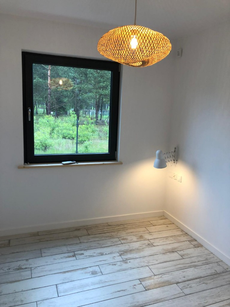 Pokój z oknem, jasną podłogą i lampą wiszącą